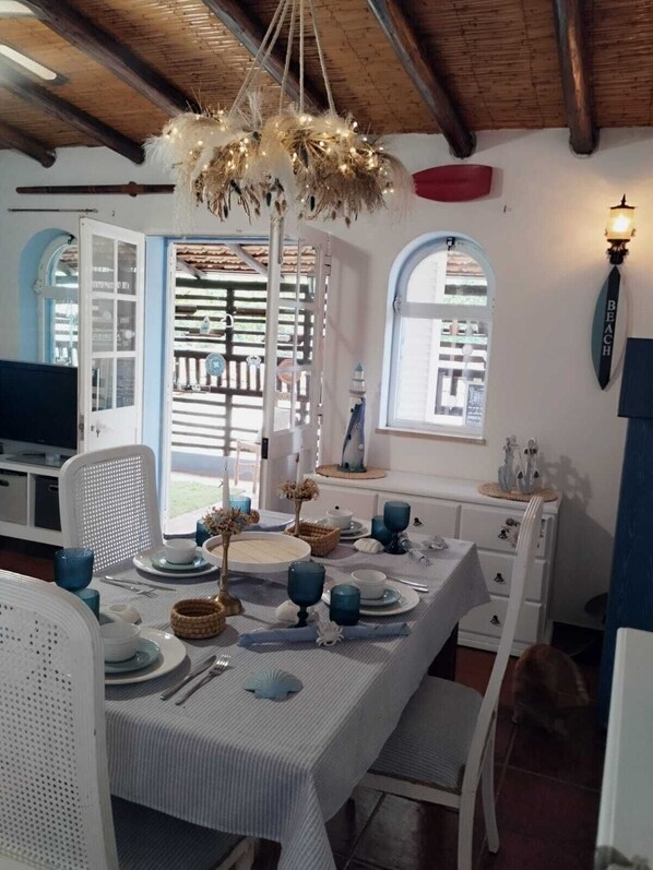 Comedor con mesa preparada para cuatro, lámpara colgante y vista al exterior por una ventana.