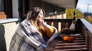 Una persona sentada en un banco con una botella de vino, un bol de fruta y calabazas sobre una mesa.