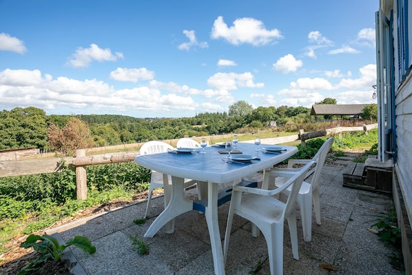 Une table de patio avec des chaises, une vue sur une zone boisée et un bâtiment en arrière-plan.