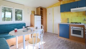 A compact kitchen with a dining area, a built-in oven, and a bench. - Mobile Home 'Entre Terre Et Mer' with Private Terrace and Private Garden (Coatascorn)
