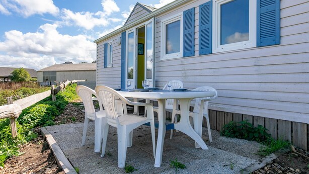 A white house with blue shutters, a patio with white plastic chairs, and a table. - Mobile Home 'Entre Terre Et Mer' with Private Terrace and Private Garden (Coatascorn)