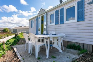 A white house with blue shutters, a patio with white plastic chairs, and a table. - Mobile Home 'Entre Terre Et Mer' with Private Terrace and Private Garden (Coatascorn)
