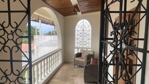 Un balcon abrité, doté d’une grille en fer forgé, d’une chaise en osier et d’une grande fenêtre ornée de vitraux.