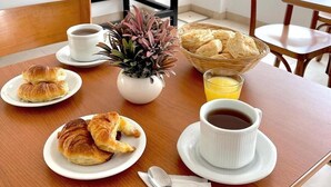 Un ambient de petit esmorzar amb croissants, una tassa de cafè, un plat de fruita i una planta sobre una taula de fusta.