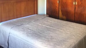 Un dormitori amb llit, armari de fusta, ventilador de sostre i un quadre al mur.