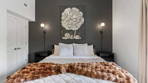 A bedroom with a bed, two bedside tables, a large floral artwork on the wall, and a fur throw on the bed.