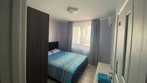 A bedroom with a bed, a bedside table, a window with curtains, and a door.
