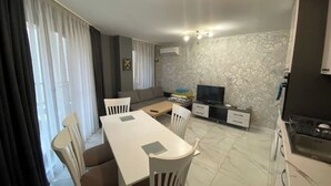 A modern living room with a dining area, a sofa, a TV, and a kitchen area.