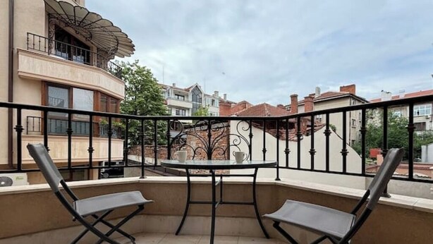 A balcony with two chairs and a table, overlooking a residential area with houses and a street.