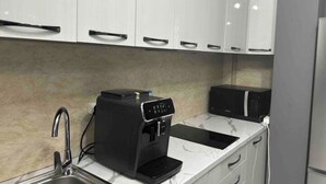 A kitchen with white cabinets, a coffee machine, a microwave, and a sink.
