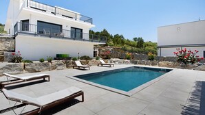 A modern house with a swimming pool, lounge chairs, and a stone wall. - Room 'Earth' with Mountain View, Shared Pool and Wi-Fi (Lourinhã)