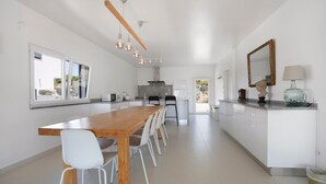 A modern kitchen with a wooden table, white chairs, and pendant lighting. - Room 'Earth' with Mountain View, Shared Pool and Wi-Fi (Lourinhã)
