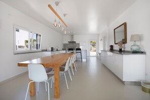 Una cocina moderna con una mesa de madera, sillas blancas e iluminación colgante.