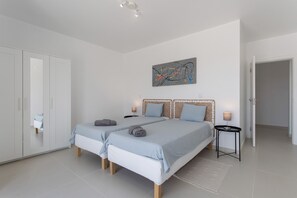 Une chambre avec deux lits, une armoire, un tableau et une petite table avec une lampe.