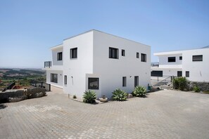 A modern two-story building with a flat roof, large windows, and a paved courtyard.