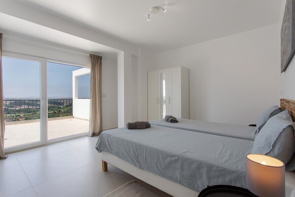 A bedroom with two beds, a wardrobe, and a balcony with a view.