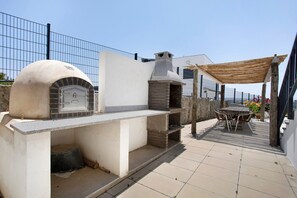 An outdoor kitchen area with a brick oven, a grill, and a dining table with chairs.