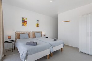 Un dormitorio con dos camas, una mesita de noche, un armario y dos cuadros abstractos en la pared.
