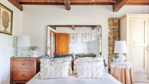 A bedroom with a wooden headboard, a large bed with patterned bedding, a nightstand with a lamp, a dresser, and a mirror reflecting the room. - Smart Panoramic Farmhouse Jacuzzi in Montecatini Alto (Montecatini alto)
