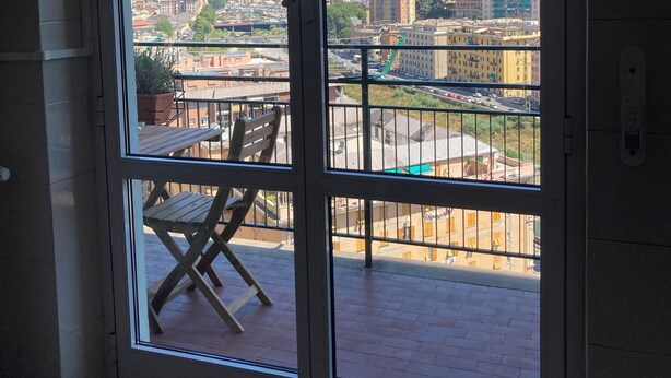 Una habitación con puerta de vidrio corrediza que da a un balcón exterior con vistas a la ciudad y colinas.