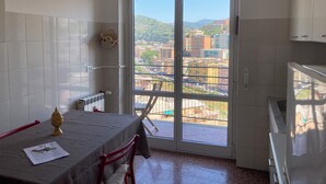 Una pequeña cocina con una mesa de comedor, una silla roja y vistas a un paisaje urbano a través de un ventanal corredero.
