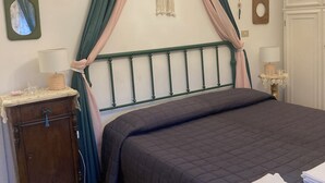 Un dormitorio con cama, mesita de noche, cómoda, un tapiz de macramé, una lámpara de araña y una pequeña decoración de pared.