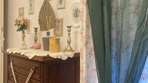 Una habitación con un aparador de madera, cortinas con motivos florales e impresiones botánicas enmarcadas en la pared.