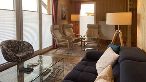 A cozy living room with a glass coffee table, two armchairs, a sofa, and a lamp.
