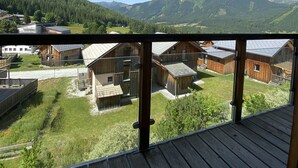 A wooden deck with a view of a rural area, including wooden buildings and a mountain range.