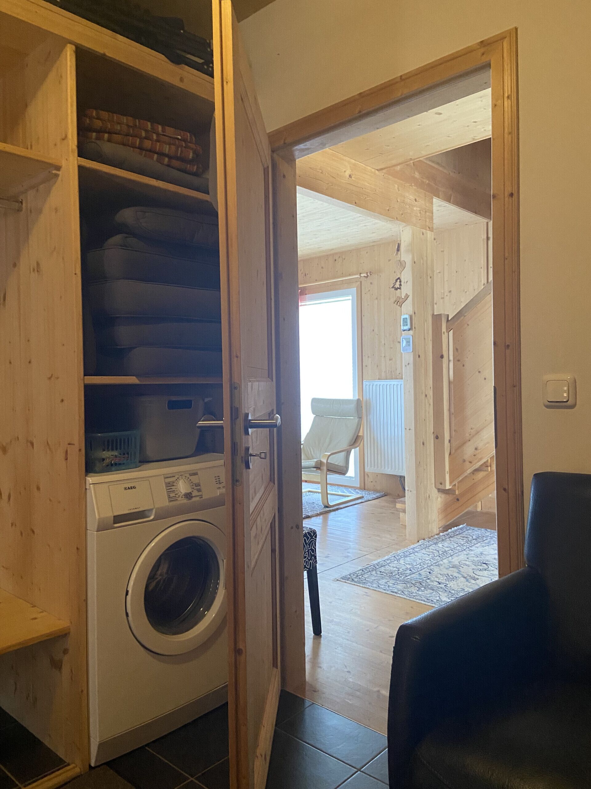 Un cuarto de lavandería con lavadora y tendedero, paredes de madera, y vistas a una sala de estar con una silla y una alfombra.