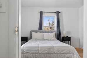 Un dormitorio con cama, mesita de noche, lámpara y ventana con cortinas.