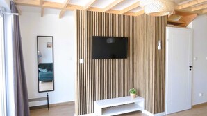 A modern room with a slatted wooden wall, a flat-screen TV, a white bench, and a door. - New holiday homes for 6 people, Niechorze (Niechorze)