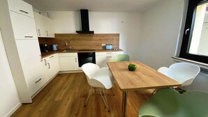 Cocina compacta con armarios blancos, encimera de madera y zona de comedor con mesa y sillas.