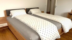 Una cama doble con colchón gris y ropa de cama blanca con diseño azul.