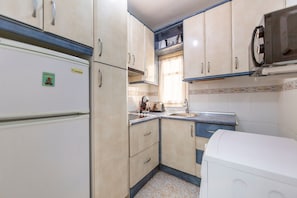 Eine kleine Küche mit Kühlschrank, Herd, Spüle und Mikrowelle.
