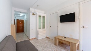 A room with a sofa, a wooden bench, a TV mounted on the wall, a cabinet with glass doors, and a door leading to another room. - Bright Apartment 'Zapillomotril' with Air Conditioning (Almería)