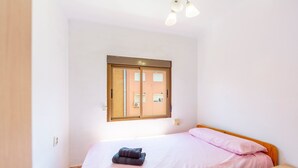 A bedroom with a bed, a wooden nightstand, a window with a view of buildings, and a ceiling light fixture. - Bright Apartment 'Zapillomotril' with Air Conditioning (Almería)