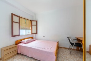 Ein Schlafzimmer mit Bett, Nachttisch aus Holz, Stuhl und Schreibtisch.
