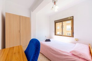 Quarto com cama, guarda-roupa, escrivaninha e janela com vista para edifícios.