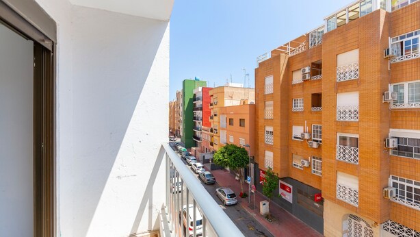 A multi-story building with balconies, a street with parked cars, and a clear sky. - Bright Apartment 'Zapillomotril' with Air Conditioning (Almería)