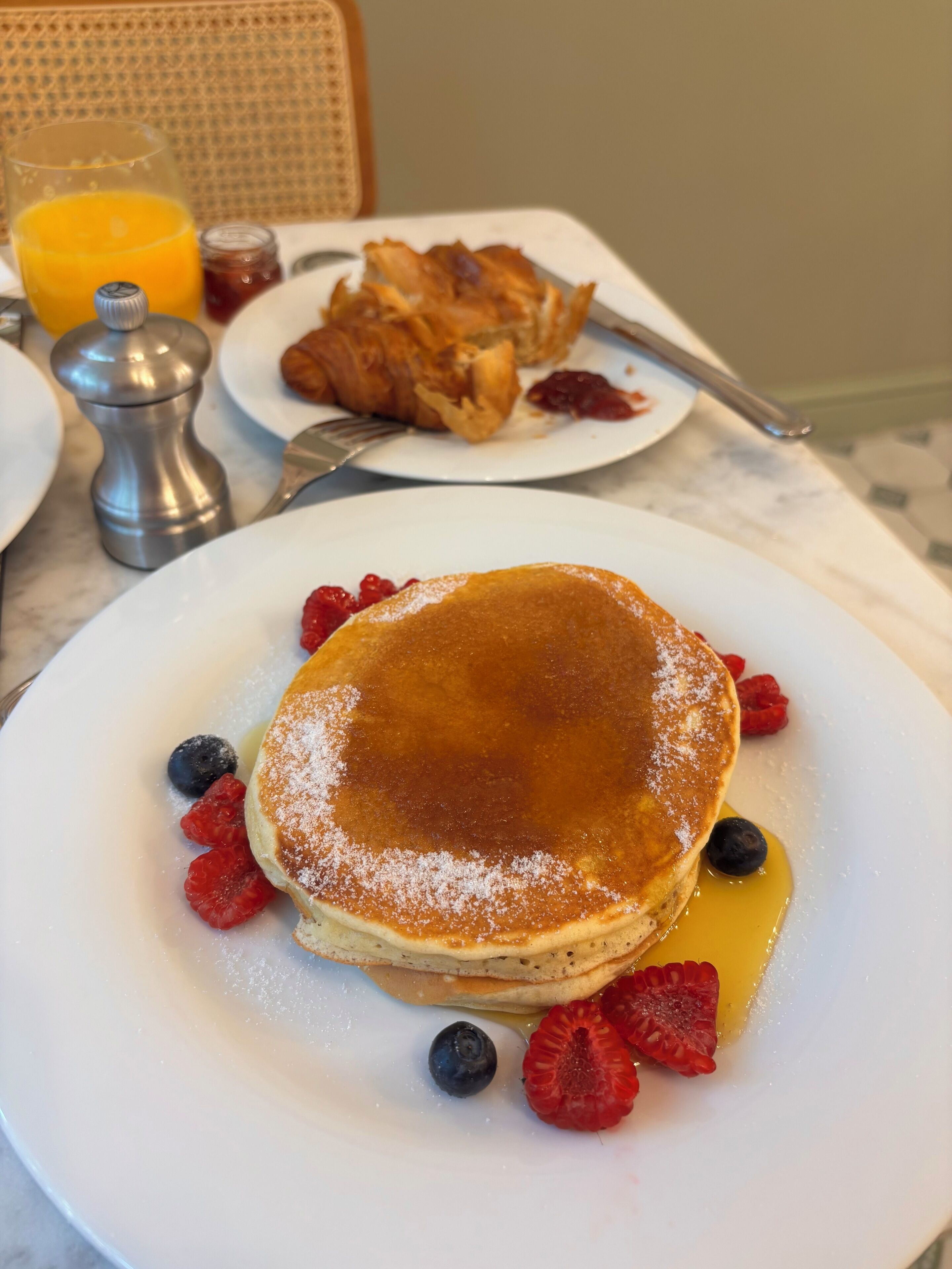 A breakfast setting with pancakes, berries, and a glass of orange juice.