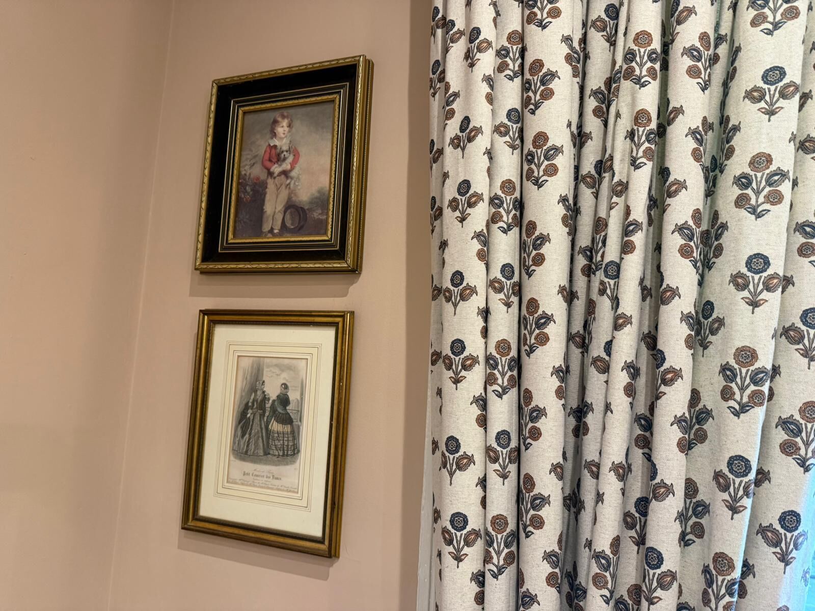 Two framed pictures on a wall and a curtain with a floral pattern.