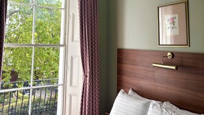 Une chambre avec une grande fenêtre, un lustre, un tableau encadré et une tête de lit en bois.