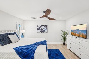 A modern bedroom with a bed, a ceiling fan, a TV, and a painting on the wall.