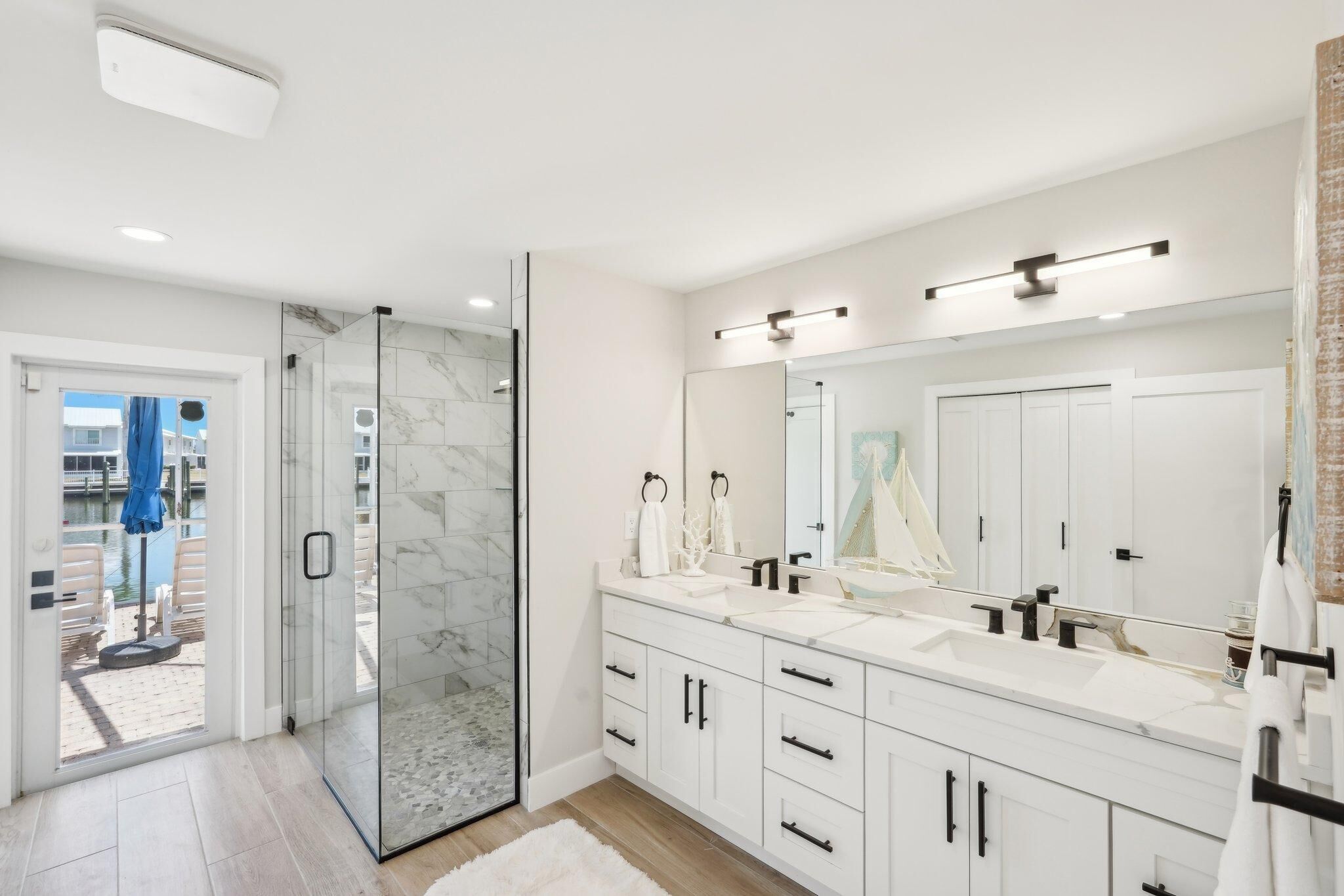 A modern bathroom with a glass shower enclosure, a large mirror, and white cabinetry.