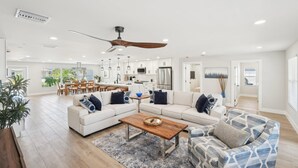 A spacious living room with a large sofa, a coffee table, and a patterned armchair. A dining area with a table and chairs is visible in the background. - Tranquility Waters (Fort Myers Beach)