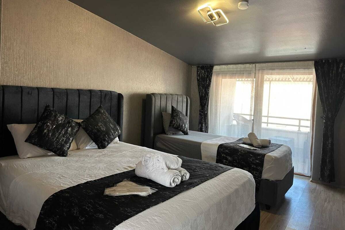 Ein Hotelzimmer mit zwei Betten, jeweils mit Kopfteil, und einem großen Fenster mit Vorhängen.