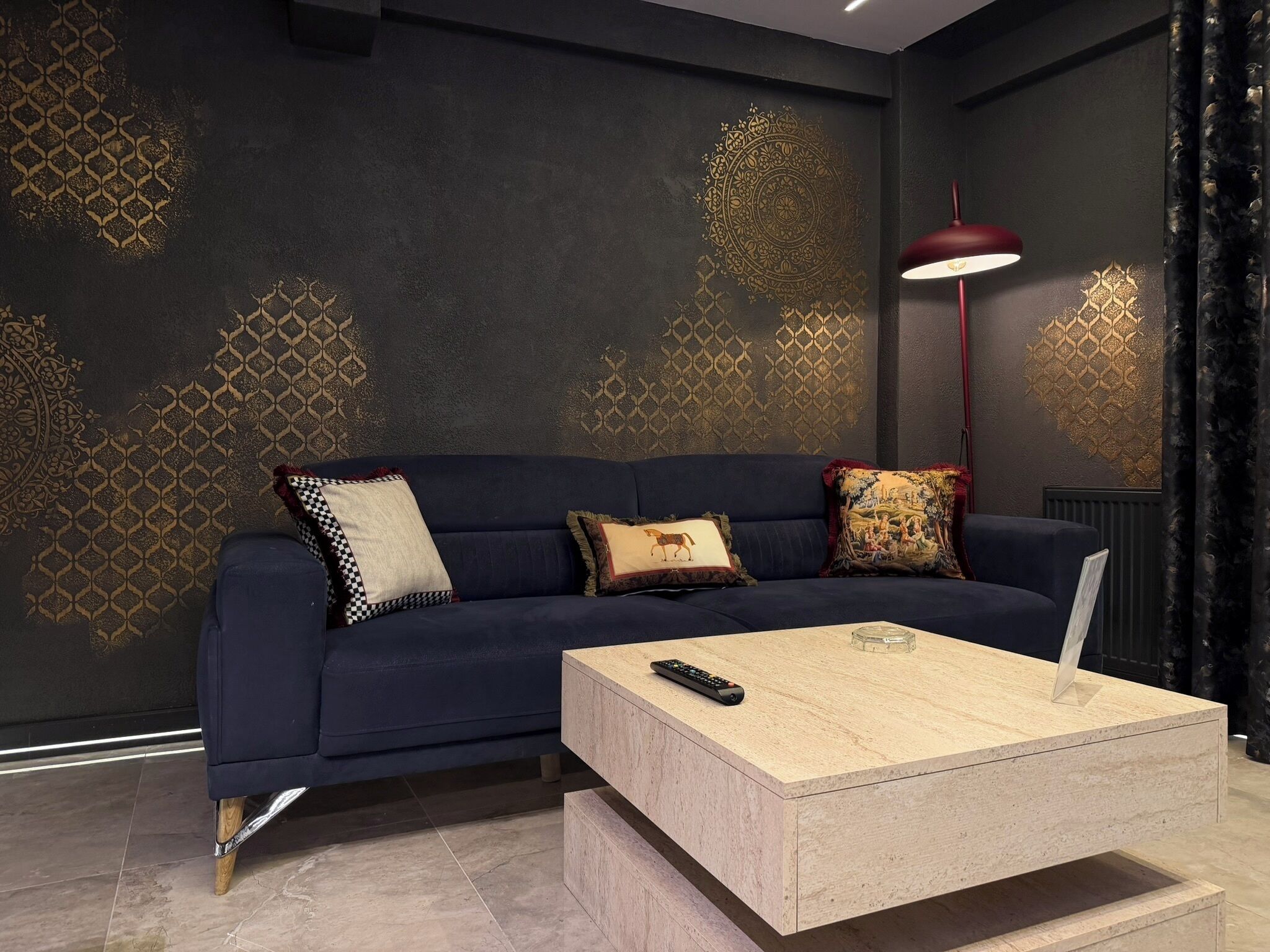 A dark blue sofa with patterned cushions, a wooden coffee table, and a red floor lamp in a modern living room.