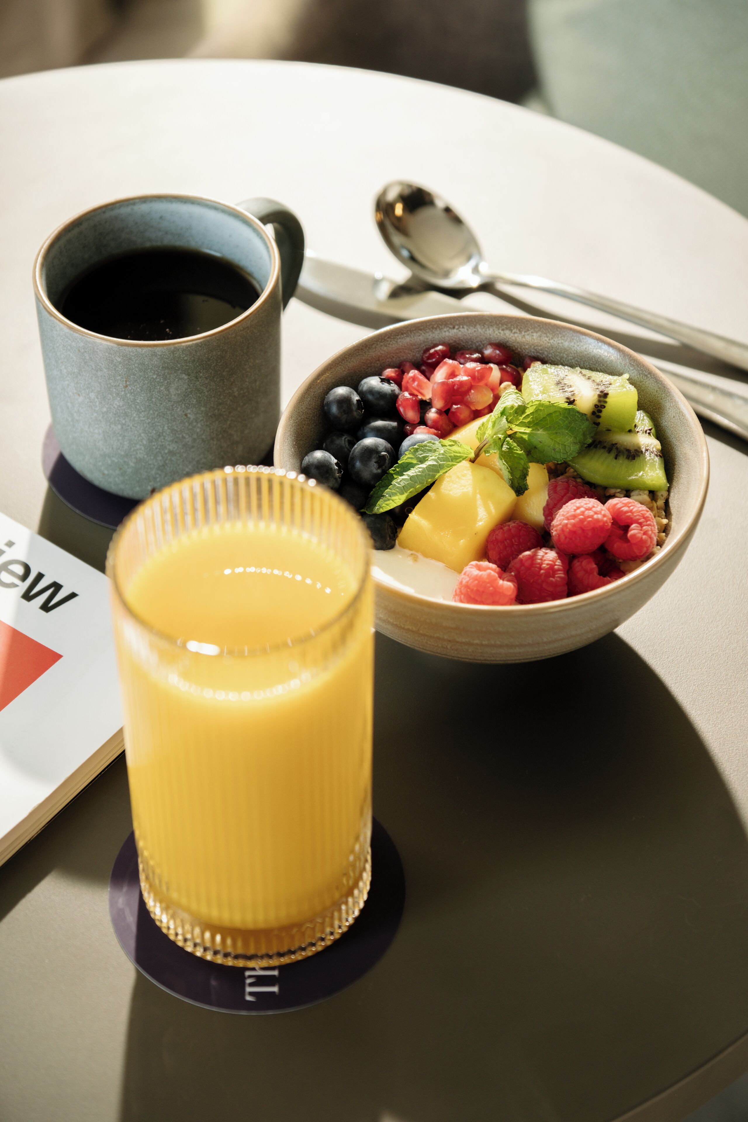 Desayuno con un bol de fruta, un vaso de jugo de naranja y una taza de café sobre una mesa.