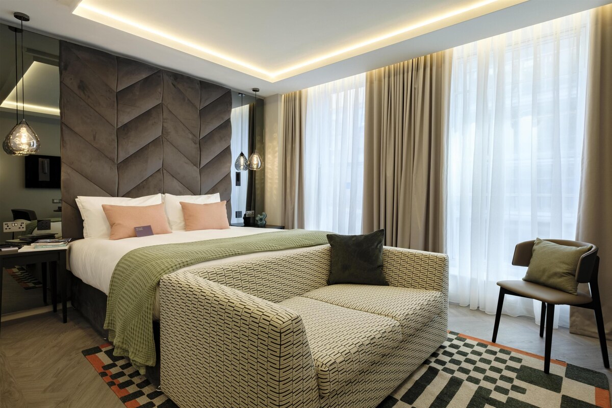 A modern hotel room with a large bed, a sofa, a chair, and a desk.